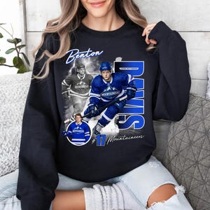 May include: Black sweatshirt featuring a collage of a hockey player in a blue uniform. The design includes the name "Benton Davis" in white script, the number "17", and the word "Mountaineers".