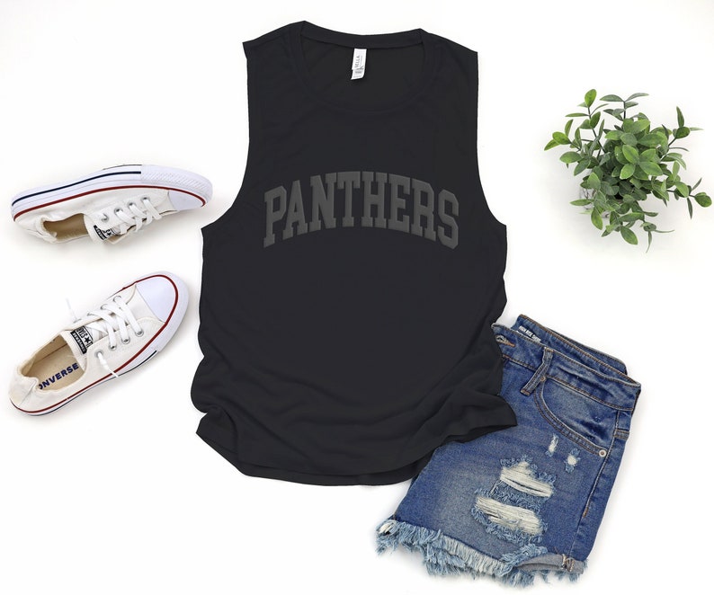 May include: Black muscle tank top with the word "Panthers" in gray arched lettering. The tank top is paired with denim shorts, white sneakers, and a small green plant.