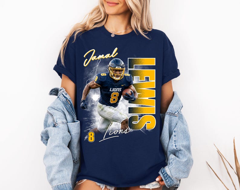 K&ouml;nnte beinhalten: Ein marineblaues Kurzarm-T-Shirt mit einem Grafikdruck eines Footballspielers in einer marine-goldenen Uniform mit der Nummer 8. Der Text lautet Jamal Lewis, Lions und die Nummer 8. Das Design enth&auml;lt Blitzeffekte und eine kr&auml;ftige gelbe Schrift.