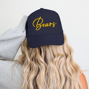 May include: A navy blue trucker hat with a gold embroidered cursive word "Bears" on the front.