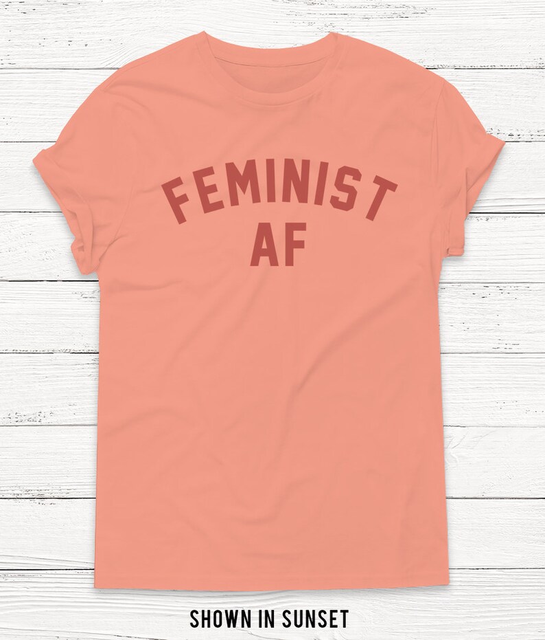 May include: A peach colored t-shirt with the text "FEMINIST AF" in a red color.