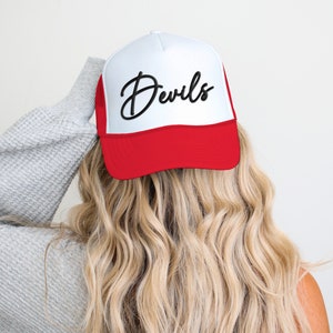 May include: A white and red trucker hat with a black cursive script that says "Devils".