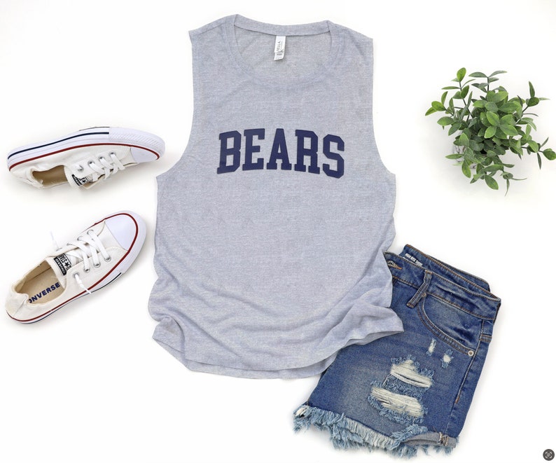 May include: A light gray sleeveless shirt with the word "BEARS" in navy blue block letters. The shirt is paired with denim shorts and white sneakers. A small green plant is also in the image.