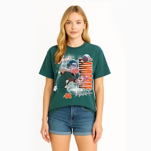 K&ouml;nnte beinhalten: Ein dunkelgr&uuml;nes Kurzarm-T-Shirt mit einem Grafikdruck eines Footballspielers in Helm und Trikot mit der Nummer 84. Der Text "Jack" und "LANDGRAF" erscheint in Orange und Wei&szlig;, zusammen mit "Woodlands Highlanders" in Schreibschrift.