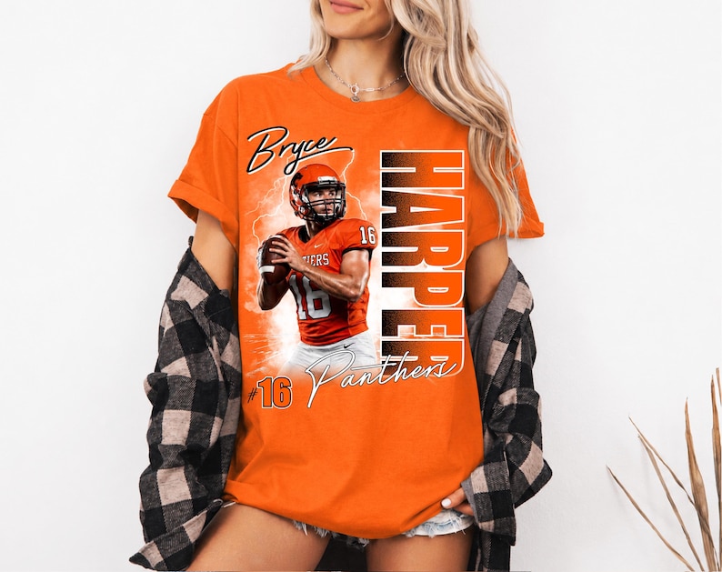 K&ouml;nnte beinhalten: Ein orangefarbenes T-Shirt mit einem Grafikdruck eines Footballspielers im orangefarbenen Trikot mit der Nummer 16, dem Text Bryce Harper und dem Wort Panthers. Das T-Shirt wird unter einem schwarz-wei&szlig; karierten Langarmhemd mit Kn&ouml;pfen getragen.