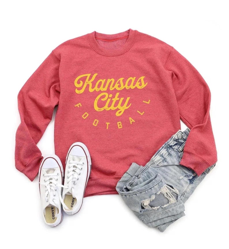 K&ouml;nnte beinhalten: Roter Pullover mit einer gelben Grafik, auf der "Kansas City Football" in einer Retro-Schrift steht.