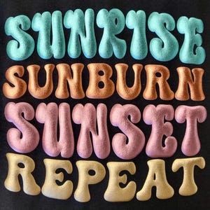 May include: Black t-shirt featuring the phrase "SUNRISE SUNBURN SUNSET REPEAT" in a retro font. The text is in blue, orange, pink, and yellow. The letters have a textured, puffy appearance.