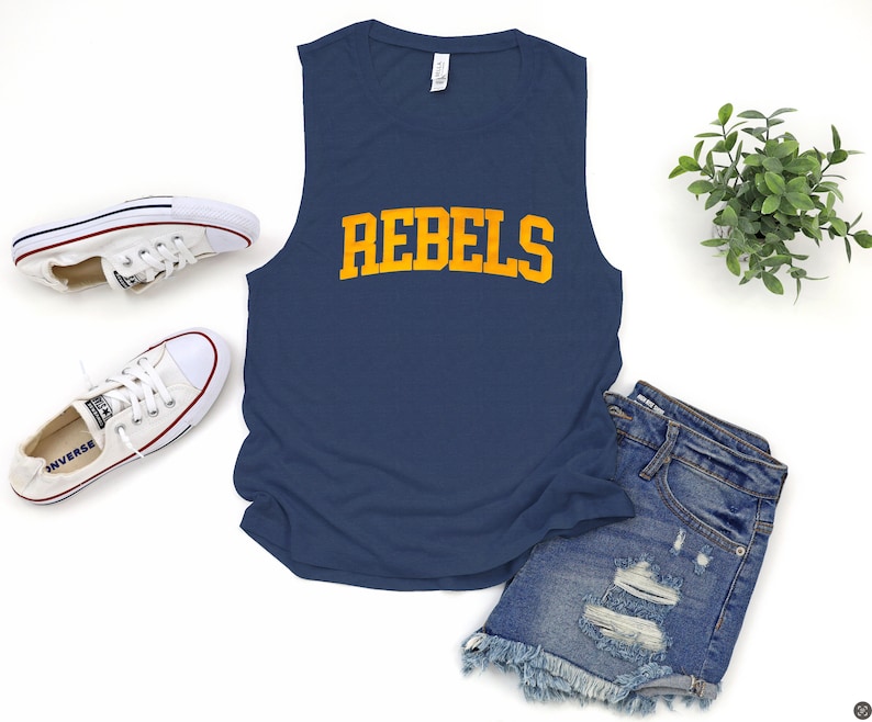 May include: Navy blue sleeveless shirt with the word "REBELS" in gold lettering. The shirt is paired with denim shorts and white sneakers. A sprig of greenery adds a decorative touch to the scene.