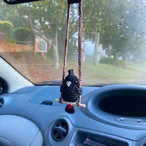 Pu&ograve; includere: Un piccolo uccellino nero all'uncinetto appeso a un cordino marrone intrecciato. L'uccello presenta un becco bianco, una piccola macchia rossa sulla coda ed &egrave; appollaiato su un bastoncino di legno chiaro che funge da altalena per l'ornamento.