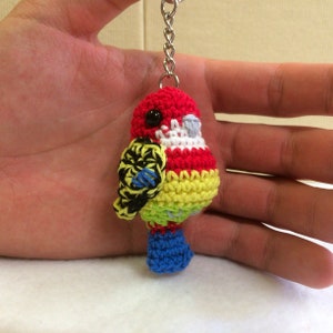 May include: A crocheted parrot keyring with red, yellow, green, blue, white and black yarn. The parrot has a black eye and a silver keyring.