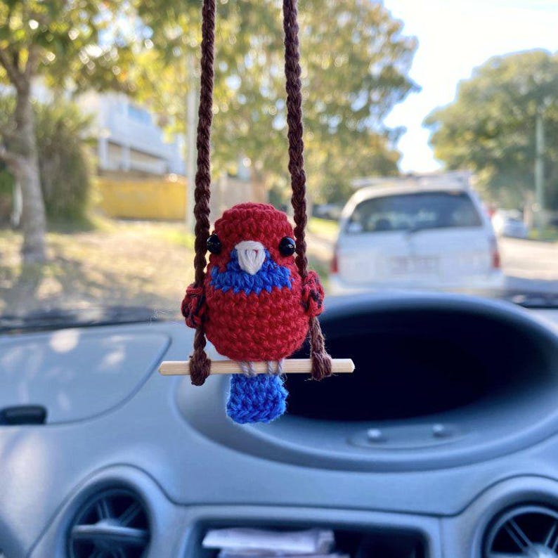 Pu&ograve; includere: Un piccolo ornamento a forma di uccellino all'uncinetto con un corpo rosso vivace, una macchia blu sul petto e una coda blu. L'uccellino ha occhi a perla neri e un becco bianco, ed &egrave; appollaiato su un bastoncino di legno orizzontale sospeso da due cordini intrecciati marroni.