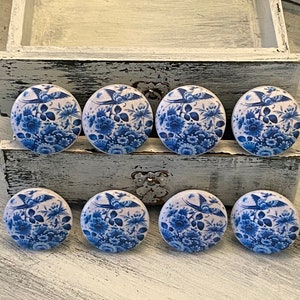 May include: Eight blue and white ceramic drawer knobs with a floral and bird design. The knobs are round and have a glossy finish.