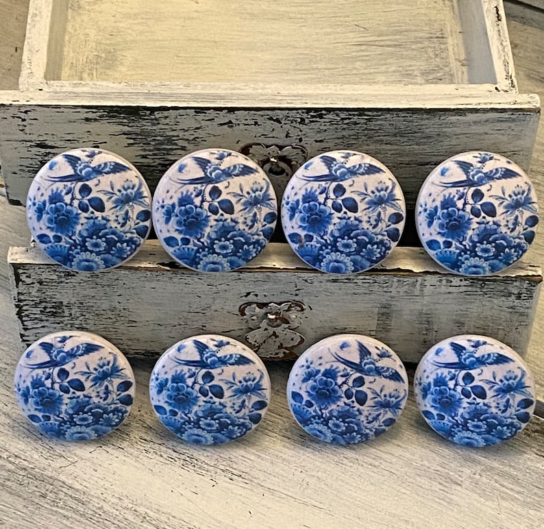 May include: Eight blue and white ceramic drawer knobs with a floral and bird design. The knobs are round and have a glossy finish.