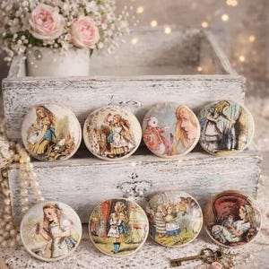 May include: Eight round decorative objects featuring illustrations from Alice in Wonderland. The illustrations depict scenes with Alice, the White Rabbit, and other characters. The objects are arranged on a white wooden tray with a bouquet of pink roses in the background.