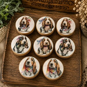 May include: Eight round wooden buttons featuring illustrations of Basset Hound puppies wearing colorful bandanas and floral or feather headpieces. The buttons are arranged on a wooden board with the text ReVampdRelics engraved at the top.