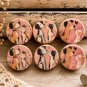 May include: A set of six circular wooden drawer knobs featuring illustrations of dogs and cats facing each other on a pink background. Each knob displays a unique pair of animals with small heart motifs, rendered in a soft, hand-drawn artistic style.
