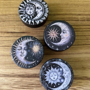 May include: Four round wooden coasters with a black background and a white sun and moon design. Each coaster features a different design of the sun and moon.
