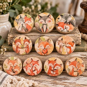 May include: A set of ten round wooden knobs featuring watercolor illustrations of foxes in various poses, including pairs cuddling, holding flowers, and holding hearts, with soft orange, gray, and cream tones on a natural wood base.