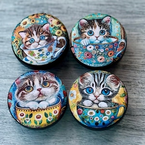 May include: Four round wooden knobs with colorful images of cats drinking tea from teacups. Each knob features a different cat with a unique design and color scheme.