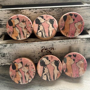 May include: Six round wooden cabinet knobs with a pink background. Each knob features a dog and cat illustration, with a heart above their heads. The dogs and cats are in various colors, including brown, black, and white.