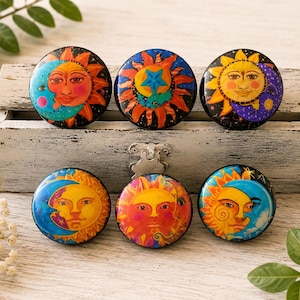 May include: Six circular cabinet knobs featuring colorful celestial illustrations of suns and moons. Each knob displays a unique artistic depiction of a sun and moon face in vibrant shades of orange, yellow, blue, and purple against dark backgrounds.