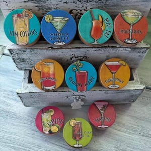 May include: Nine colorful round coasters with illustrations of different cocktails, including Tom Collins, Vodka Gimlet, Tequila Sunrise, Bloody Mary, Mai Tai, Margarita, Cosmopolitan, Mojito, Long Island Ice Tea, and Martini.