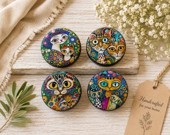 May include: Four circular cabinet knobs featuring colorful, intricate illustrations of cats with large eyes and patterned backgrounds. Each knob displays a unique artistic cat design with vibrant hues of blue, green, yellow, and orange in a mosaic style.