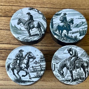 May include: Set of four black and white ceramic bottle stoppers featuring cowboys riding horses in various poses against a landscape background.