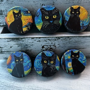 May include: Six round black buttons with a black cat image on each. The cat is in a starry night scene with yellow and blue colors.