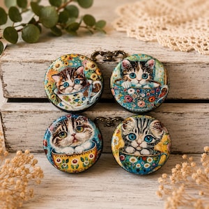 May include: Four round, decorative magnets featuring adorable kittens in teacups. Each magnet has a unique kitten design with blue eyes, set against a colorful floral background. The magnets are attached to a white wooden box.