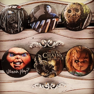 May include: Six round horror movie themed buttons. The buttons feature characters from Friday the 13th, The Texas Chainsaw Massacre, and Child's Play. The buttons are black, white, red, and blue.