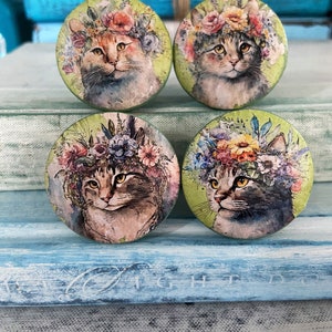 May include: Four round wooden knobs with a green background and a watercolor image of a cat wearing a flower crown.