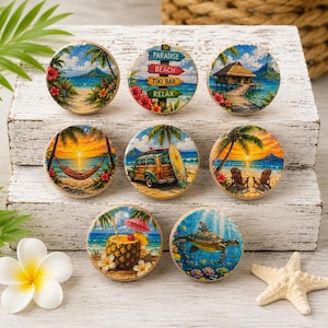 May include: A collection of round wooden decorative knobs with tropical beach scenes. Each knob features a different image, including palm trees, sunsets, a tiki bar sign, a turtle, and a pineapple drink. The knobs are arranged on a white wooden surface.
