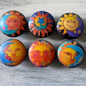 May include: Six round wooden knobs with colorful images of the sun and moon. The images are whimsical and feature a variety of colors, including yellow, orange, blue, and green.