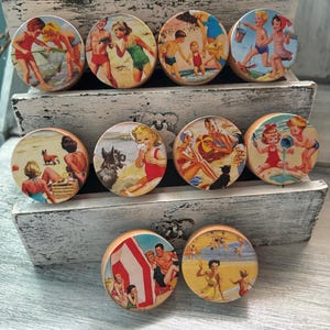 May include: Nine round wooden knobs with vintage images of people enjoying the beach. The images feature people in swimsuits, playing in the sand, and swimming in the ocean. The knobs are perfect for adding a touch of vintage charm to any home.
