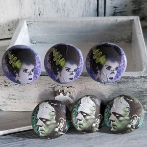 May include: Six round, ceramic drawer knobs with images of Frankenstein's monster and his bride. The knobs are purple, green, and black with white accents.