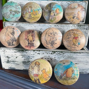 May include: Set of 9 Winnie the Pooh themed wooden knobs with various scenes featuring Winnie the Pooh, Piglet, and other characters from the Hundred Acre Wood. The knobs are painted in a variety of colors, including yellow, red, blue, green, and brown.