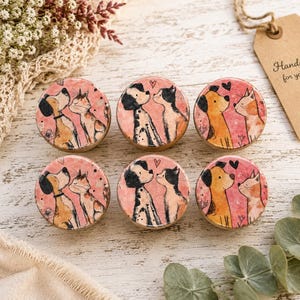 May include: Six round wooden drawer knobs featuring watercolor illustrations of dogs and cats facing each other on a pink background. Each knob displays a unique pair of pets with small hearts. A brown paper tag reads Handcrafted for your home.