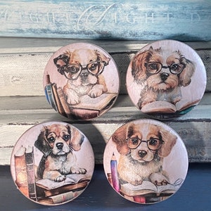 May include: Four round wooden knobs with a light pink background and a picture of a dog wearing glasses and reading a book. The dogs are all different breeds and have different colored fur. The knobs are perfect for adding a touch of whimsy to any room.