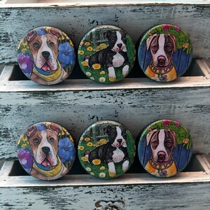 May include: Six round wooden knobs with colorful images of dogs with flowers. The dogs are all different breeds and have different expressions.