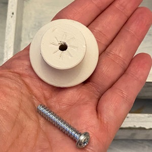 May include: White ceramic knob with a screw for attaching to a drawer or cabinet. The screw is silver and has a flat head.