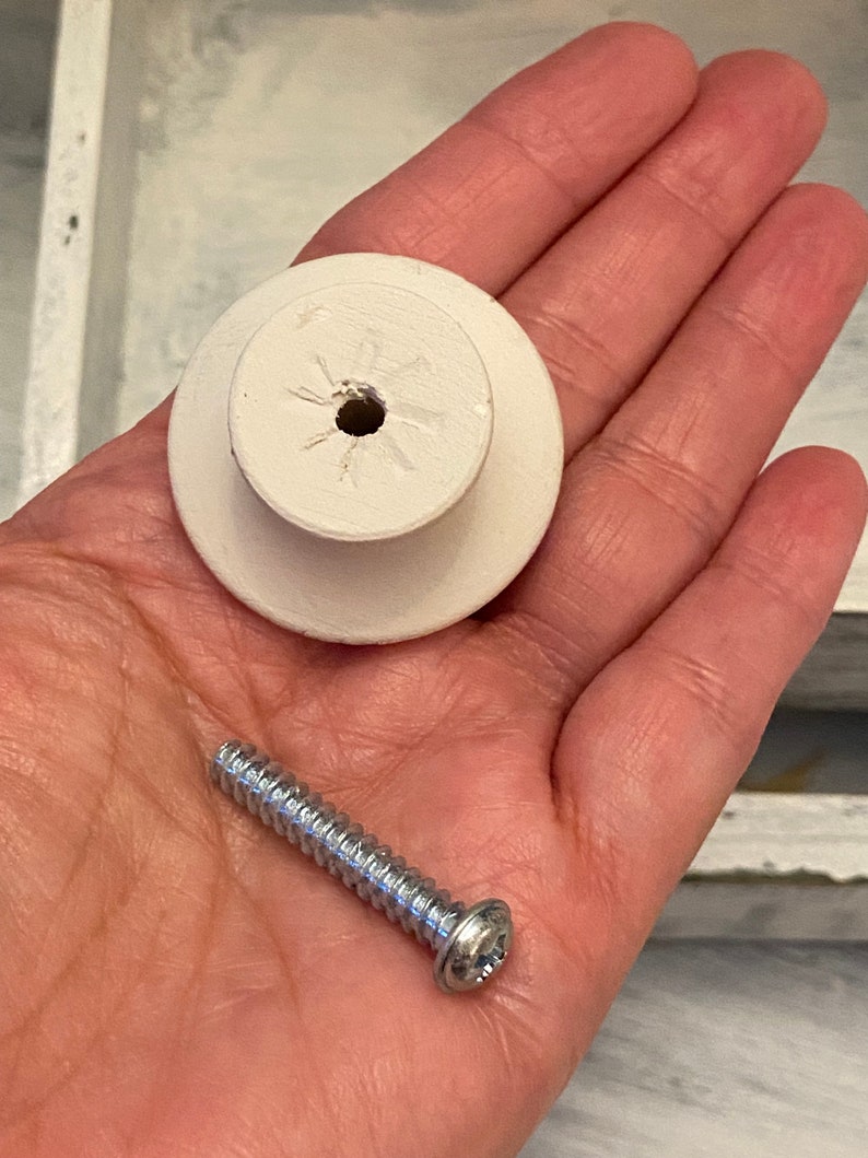 May include: White ceramic knob with a screw for attaching to a drawer or cabinet. The screw is silver and has a flat head.