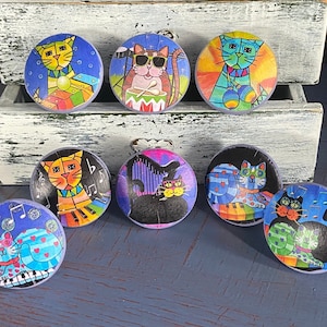 May include: Set of 8 colorful cat-themed cabinet knobs with musical notes and instruments. The knobs are made of ceramic and have a glossy finish.