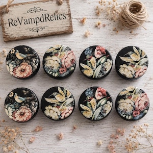 May include: Eight round black knobs arranged in two rows, each featuring a detailed floral and hummingbird design in shades of pink, yellow, green, and blue. A wooden sign with the text ReVampdRelics is positioned above the knobs.