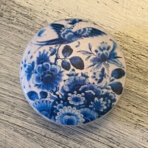 May include: A round, white ceramic knob with a blue and white floral design. The design features a bird, flowers, and leaves.