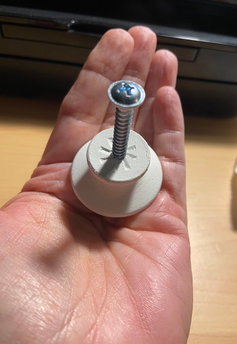 May include: White ceramic knob with a silver screw. The knob has a star-shaped design on the top.