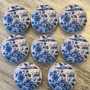 May include: Nine blue and white ceramic knobs with a floral and bird design. The knobs are round and have a smooth surface.