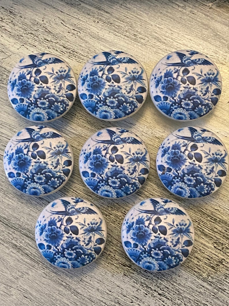 May include: Nine blue and white ceramic knobs with a floral and bird design. The knobs are round and have a smooth surface.