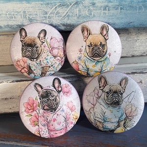 May include: Four round ceramic knobs with images of French Bulldogs wearing different outfits. The knobs are painted in pastel colors with floral designs.
