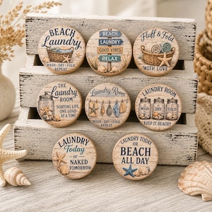 May include: A collection of nine round wooden laundry room signs with beach-themed designs. Each sign features text like "Beach Laundry" and "Laundry Today," along with images of seashells, starfish, and laundry-related items. The signs are displayed on a rustic wooden shelf.